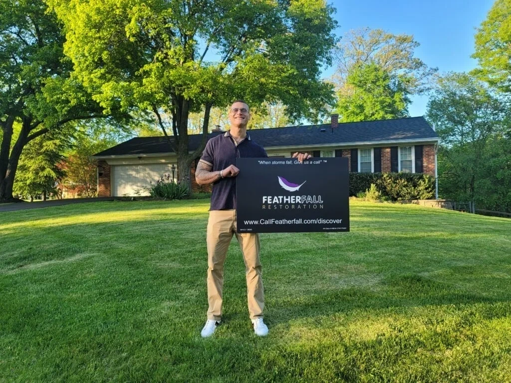 Homeowner holding FEATHERFALL yard sign on lawn