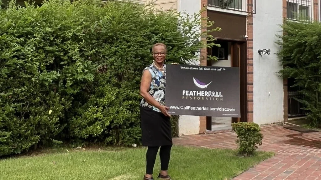 Customer holding FEATHERFALL yard sign after siding replacement