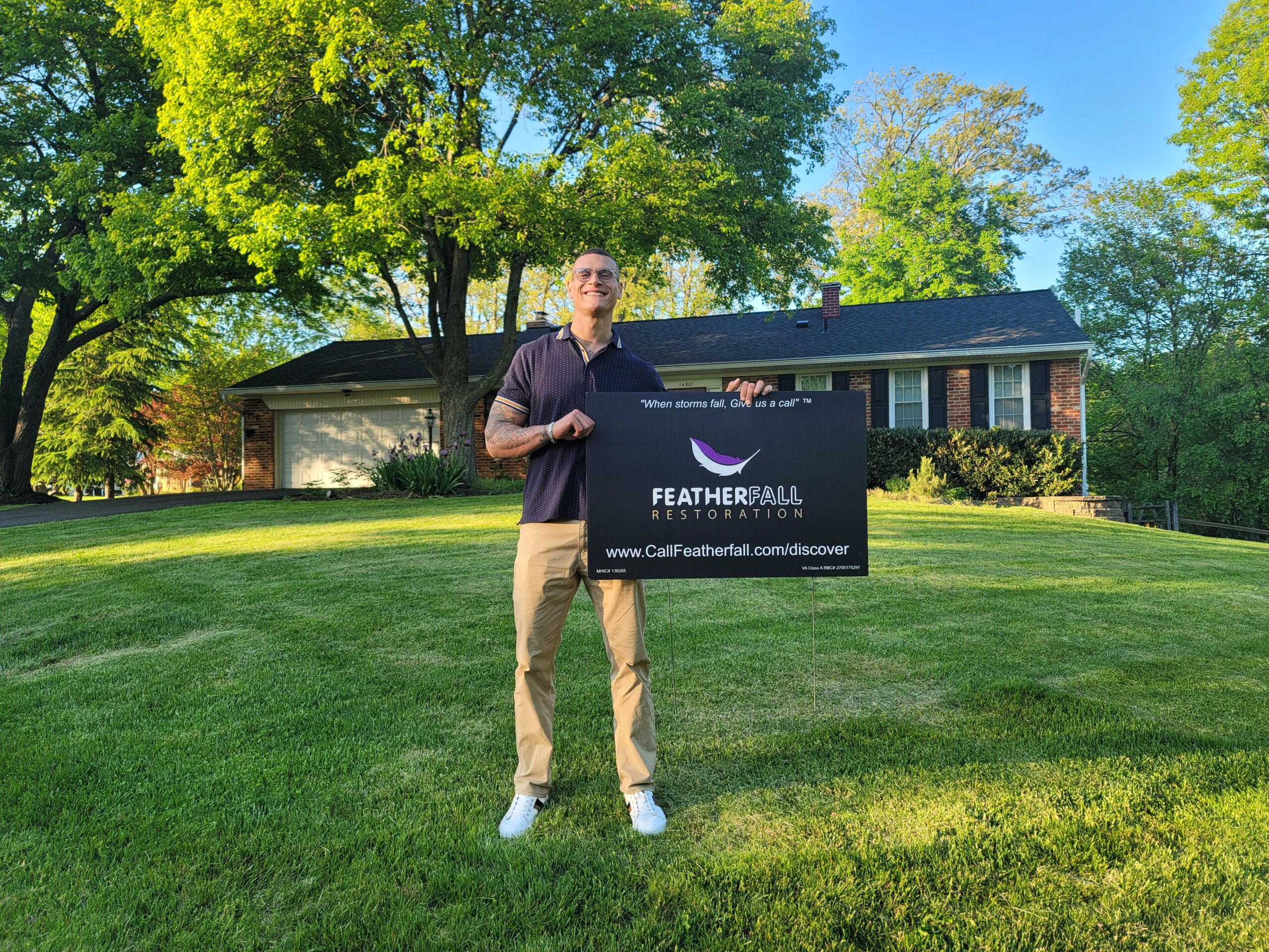 A Featherfall rep holding a Featherfall sign in front of a house after a siding job was approved by insurance.